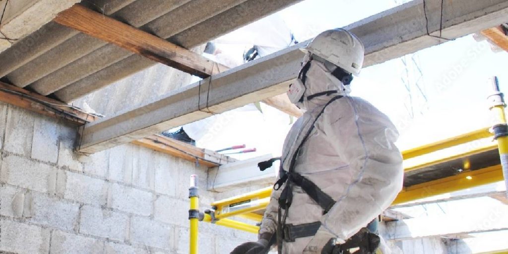 A professional asbestos remover in protective gear meticulously cleaning an asbestos roof