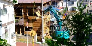 A large excavator in the process of safely demolishing a residential house.