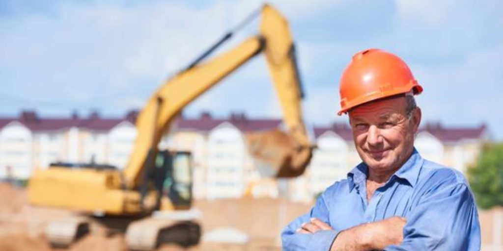 Demolition man standing confidently in front of an excavator. Learn the art of operating an excavator with our blog post