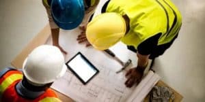 A group of demolition professionals gathered around blueprints, discussing plans for the upcoming demolition of a house.