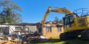 "Powerful machinery demolishing a house, creating a cloud of dust and debris