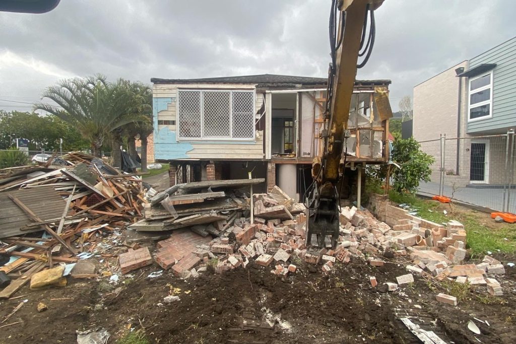 Excavator actively demolishing a residential building in an Australian suburb